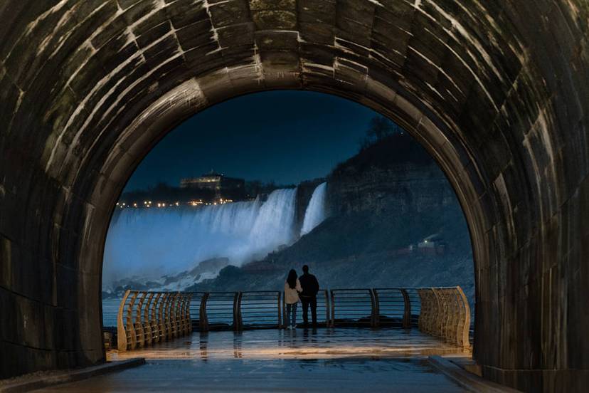 Couple standing inside a tunnel, looking out at Niagara Falls at night.