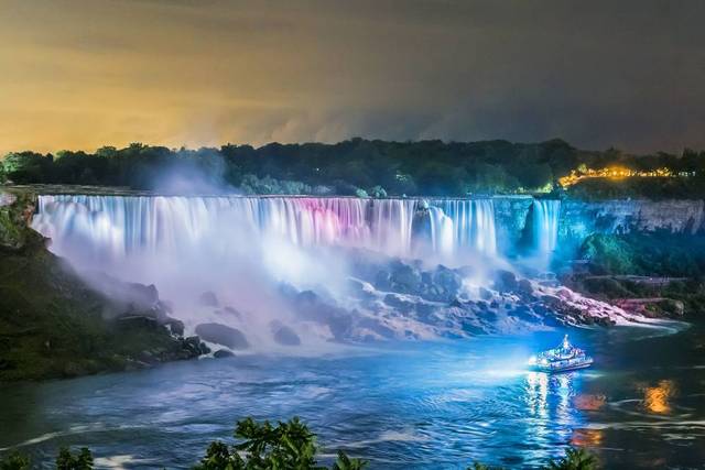 Niagara City Cruises boat with illuminated Niagara Falls at night.