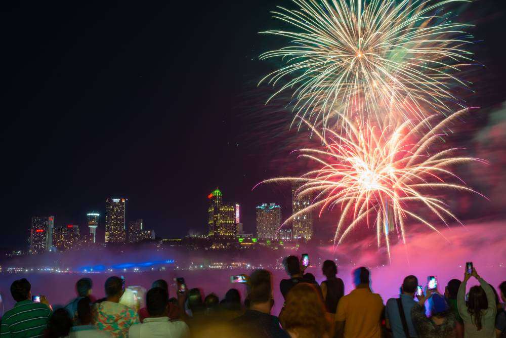 Visitors capturing fireworks over Niagara Falls at night.